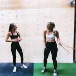 Hannah and Hannah in sports gear standing in a gym laughing, looking at each other.