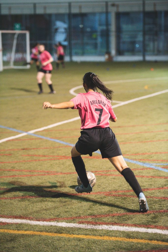 girl playing soccer in a pink jersey and black shorts, number 7 with the soccer ball running forwards