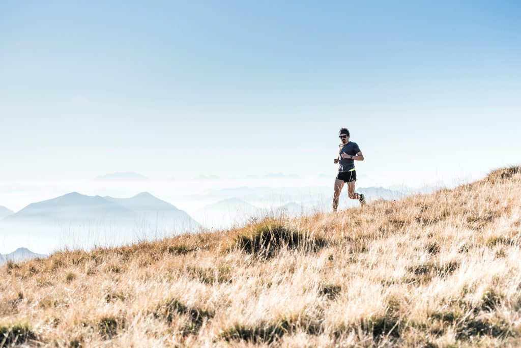 person running down a grassy hill with a blue sky and mountains in the background