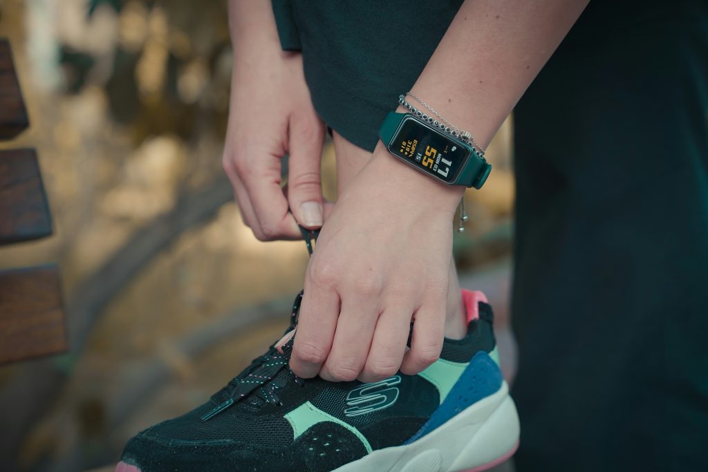  Close up of a female caucasian's hands tying their running shoe. You can see their watch is showing numbers on a small screen.