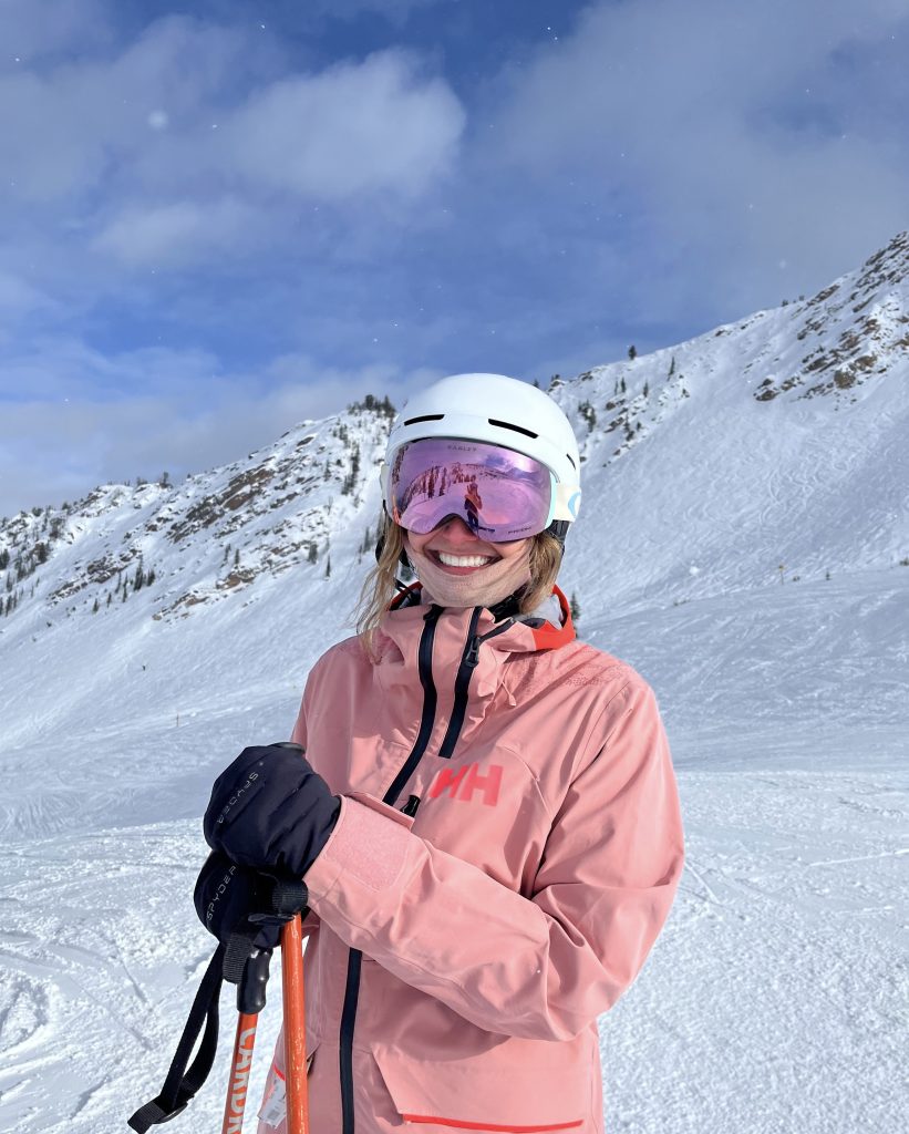 sarah in her ski gear in a pink jacket and goggles and white helmet smiling at the camera