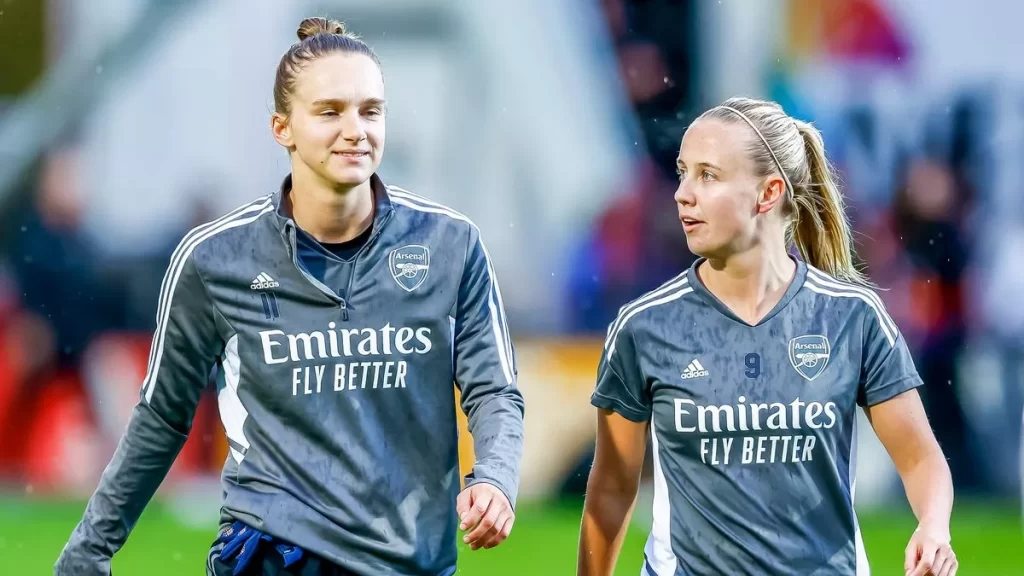 Beth Mead and Vivianne Miedema in Arsenal blue jerseys walking on the field.